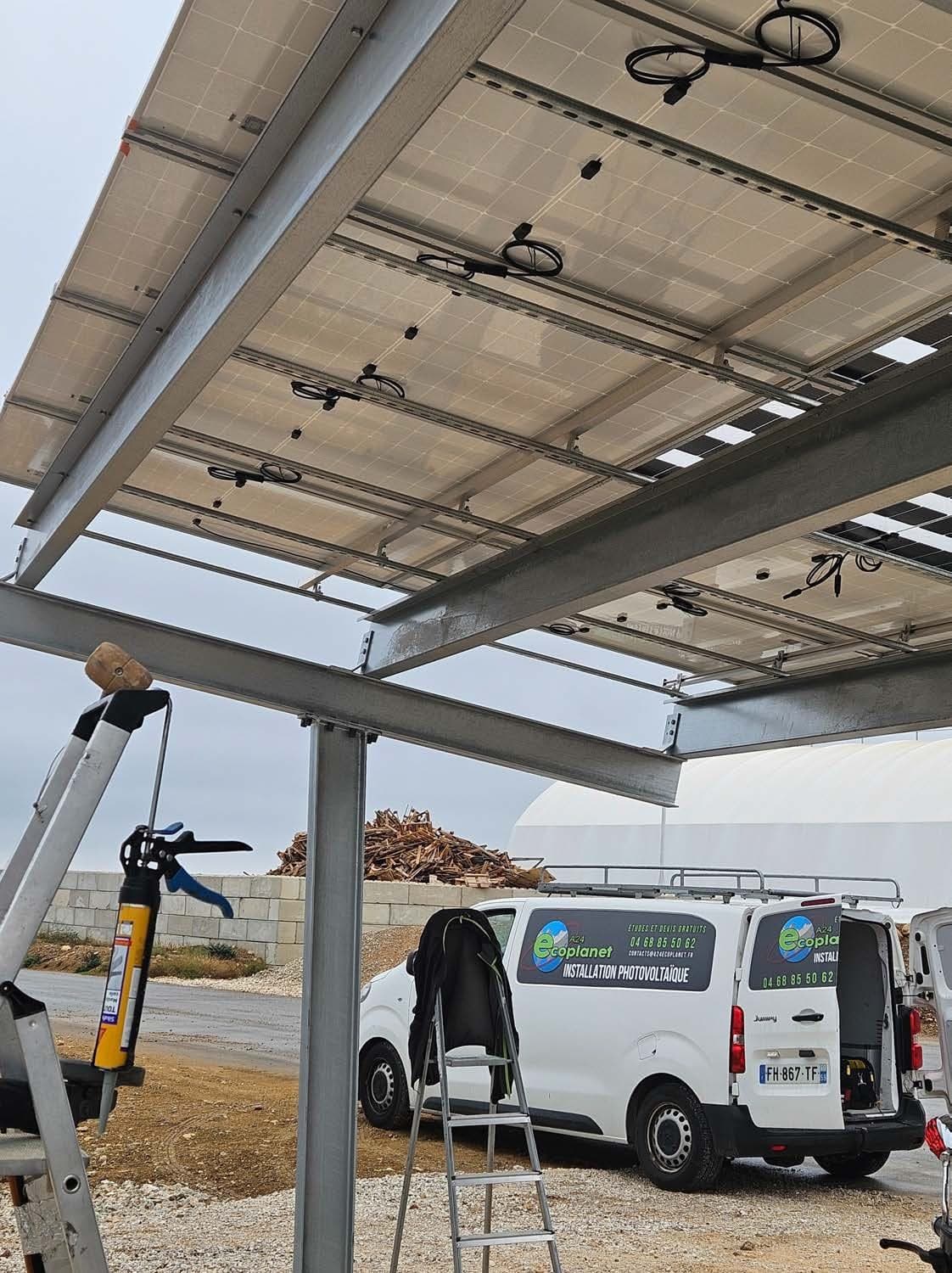 Technicien Ecoplanet France sous une ombrière photovoltaïque, véhicule d'intervention à proximité